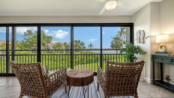 A balcony with wicker furniture, a round table, and a view of a green landscape.