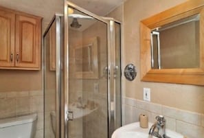 A bathroom with a glass shower enclosure, a sink, and wooden cabinets.