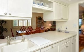 A kitchen with white cabinetry, a sink, and a countertop. There is a dining area with a table and chairs visible in the background.