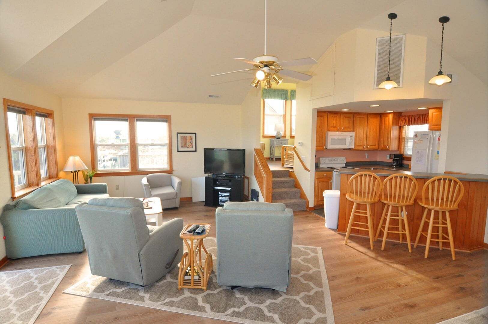 A living room with a sofa, chairs, a TV, and a kitchen with wooden cabinets and a bar area.