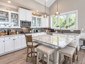 Une cuisine moderne avec des meubles blancs, un grand îlot central doté de tabourets et une vue sur la verdure à l’extérieur.