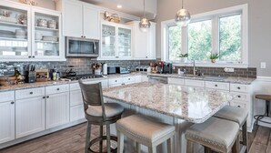 Una cocina con gabinetes blancos, encimera de granito y una isla grande con taburetes de bar.