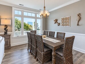 Une salle à manger avec une table en bois et des chaises en osier, un lustre et des œuvres d’art décoratives accrochées au mur.