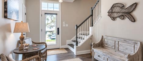 A living room with a sofa, a dining table with chairs, a lamp, a staircase, and a wall-mounted decorative piece.