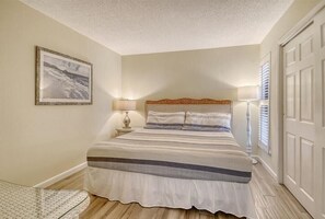 A bedroom with a bed, a nightstand, a lamp, a framed picture on the wall, and a door. - Firethorn 510- 2 BR, 1.5 BA ground floor unit close to pool (Sarasota)