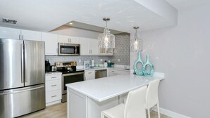 Une cuisine moderne dotée d’appareils électroménagers en acier inoxydable, de meubles blancs et d’un îlot central avec des tabourets de bar.