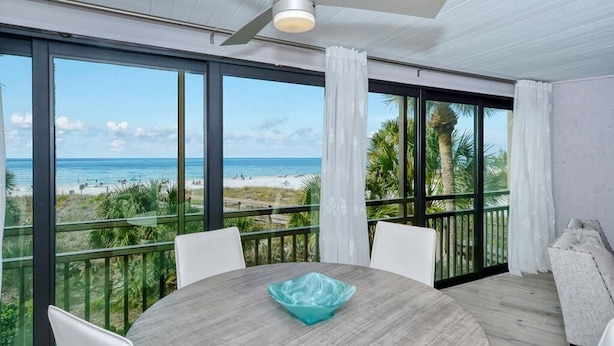 Un balcon donnant sur la plage, une table ronde avec un saladier en verre et des chaises blanches.