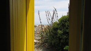 A yellow door leading to a beach path with a view of the ocean and some vegetation. - Gorgeous Character Bach (Punakaiki)
