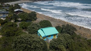 A coastal house with a turquoise roof, surrounded by dense greenery and a rocky shoreline. - Gorgeous Character Bach (Punakaiki)