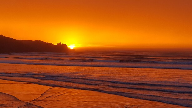 A sunset over the ocean with waves approaching the shore. - Gorgeous Character Bach (Punakaiki)