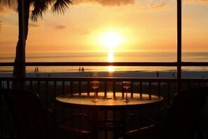 Vista al atardecer desde un balcón con mesa y sillas, con vista al océano.