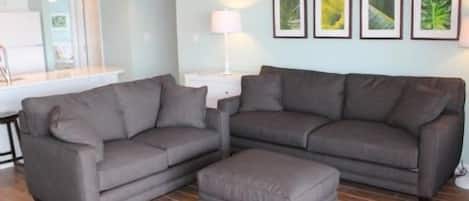 A living room with two sofas and an ottoman, a small table, and framed pictures on the wall.