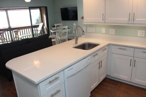 A kitchen with white cabinets, a stainless steel sink, and a built-in dishwasher. - Firethorn 321- 2 bedroom 2 bath enjoy a fabulous direct beach front view from this 2nd story walk up (Sarasota)