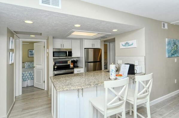 A modern kitchen with white cabinets, granite countertops, stainless steel appliances, and a breakfast bar with white chairs.