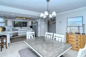 Une cuisine moderne avec des meubles blancs, un îlot central et un coin repas comprenant une grande table et des chaises.