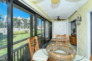 A balcony with wicker chairs and a glass table, overlooking a residential area with houses and a lawn.