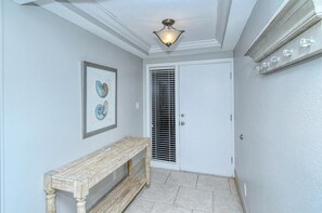 Un couloir avec un banc, une porte dotée d’une grille d’aération et un luminaire au plafond.