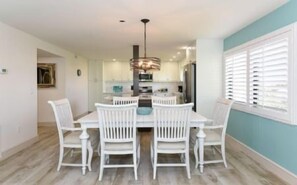 A dining area with a white table and chairs, a hanging light fixture, and a window with blinds.