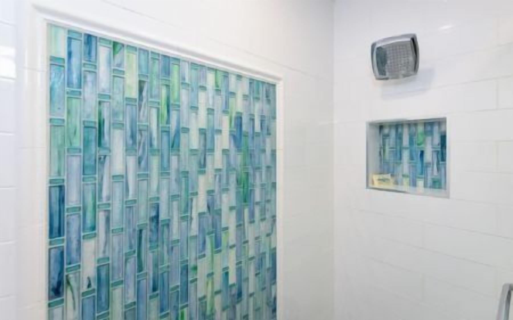 Kylpyhuone, jossa on suihkualue, lasiovi ja pieni hylly, jossa on hygieniatuotteita.