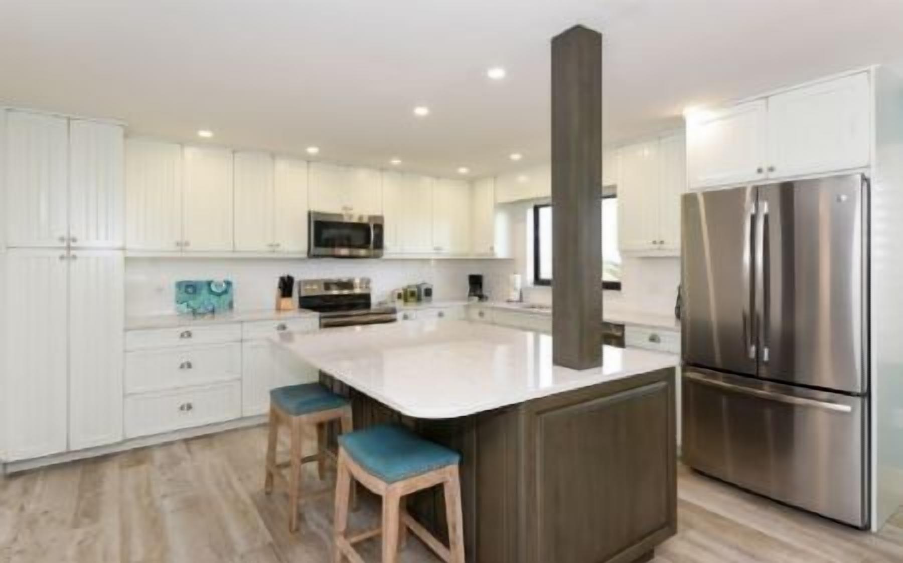A modern kitchen with white cabinets, stainless steel appliances, and a central island with stools.
