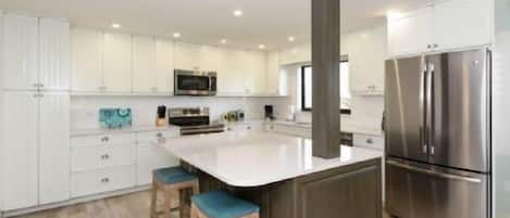 Une cuisine moderne avec des meubles blancs, des appareils en acier inoxydable et un îlot central doté de tabourets.
