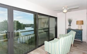 A room with a sliding glass door leading to a balcony, a ceiling fan, a lamp, and a sofa.
