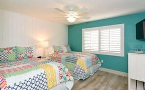 A bedroom with two beds, a ceiling fan, a window with blinds, and a TV on the wall.