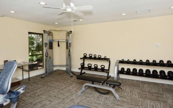 A gym with exercise equipment, a ceiling fan, and a wall-mounted dumbbell rack.