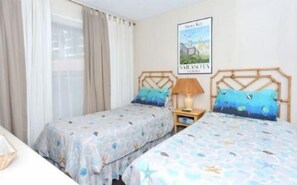 A bedroom with two beds, a nightstand, a lamp, and a poster on the wall.