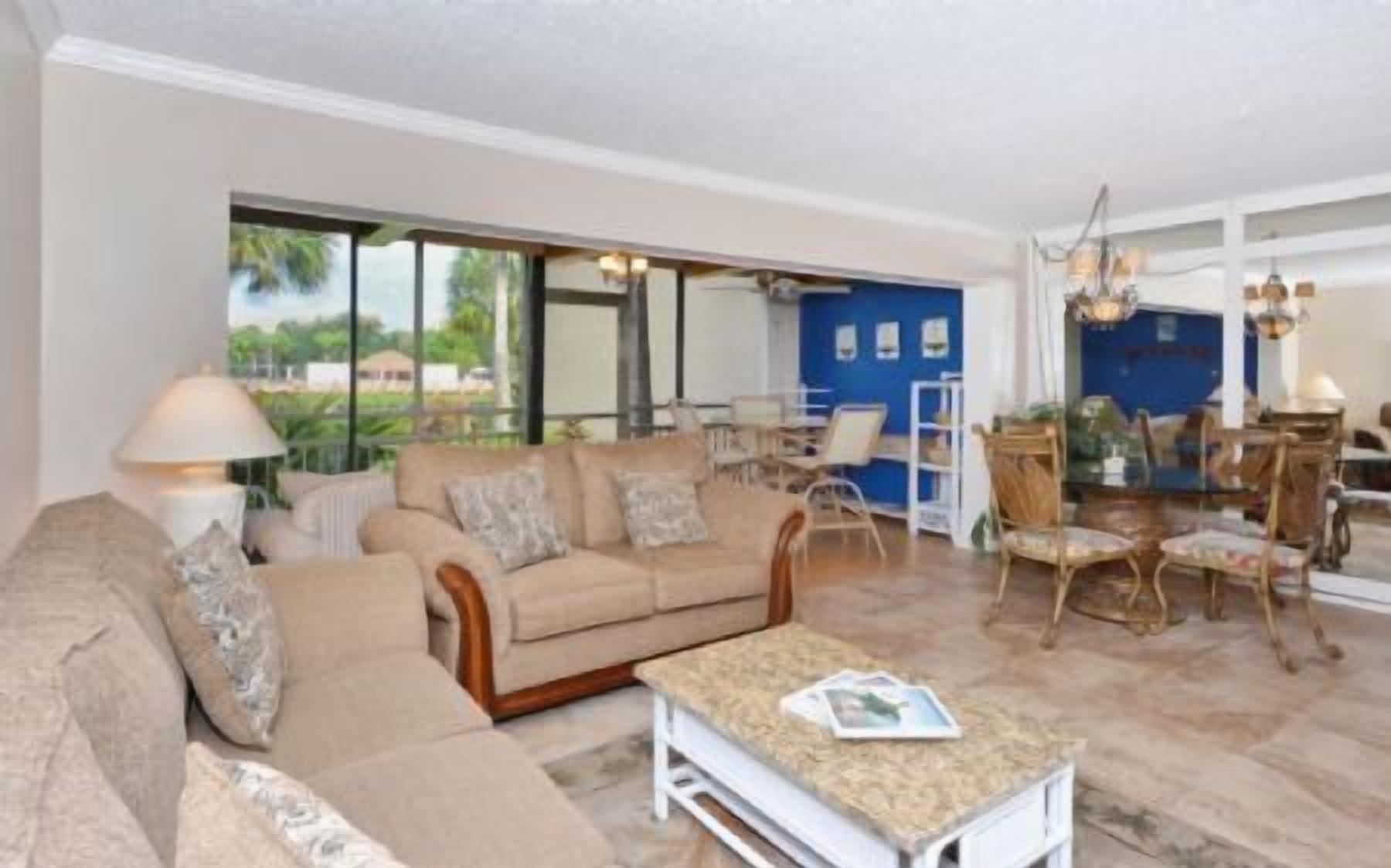 A spacious living room with a beige sofa, a coffee table, and a dining area with chairs and a table.