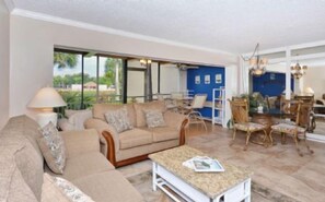 A spacious living room with a beige sofa, a coffee table, and a dining area with chairs and a table.