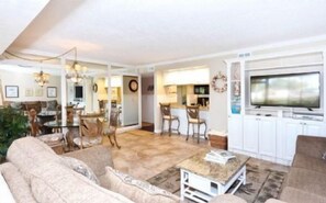 A spacious living room with a large television, a dining area with chairs, and a kitchen area with cabinets. - Firethorn 613- Ground floor 2 bed / 1.5 bath unit just steps to pool and boat docks (Sarasota)
