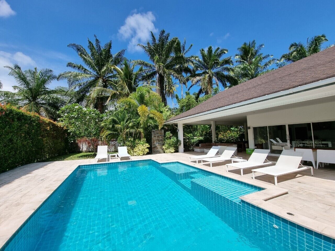 Une piscine rectangulaire à l ’eau d’un bleu cristallin, entourée de chaises longues blanches.