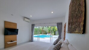 Een slaapkamer met een groot bed, een flatscreen televisie, een houten hoofdbord en uitzicht op een zwembad.