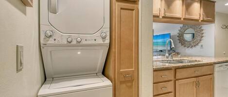 A compact kitchen with wooden cabinets, a built-in dishwasher, and a large window above the sink.