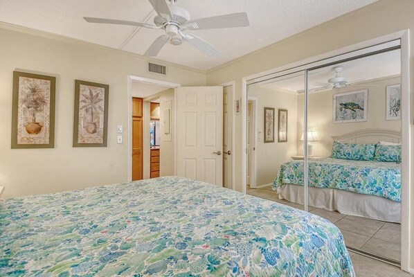A bedroom with a large bed, a second bed, a ceiling fan, and a door leading to a bathroom. - Firethorn 722- 2nd floor unit. 2 bedroom and 1.5 baths overlooking canal w/private beach access (Siesta Key)