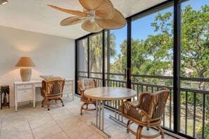 Ein Balkon mit Korbmöbeln und einem großen Ventilator, mit Blick auf einen Garten mit Bäumen.