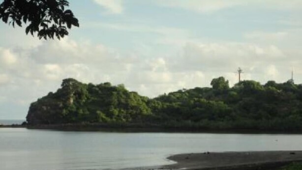 Un paisaje costero con una pequeña isla cubierta de vegetación, un mar tranquilo y un cielo despejado.