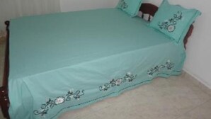 Una cama con colcha y almohadas color turquesa, un cabecero de madera y una pared blanca con una ventana.