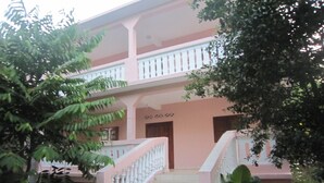Un edificio de dos pisos con fachada rosa, un balcón blanco y una escalera que conduce a la entrada.