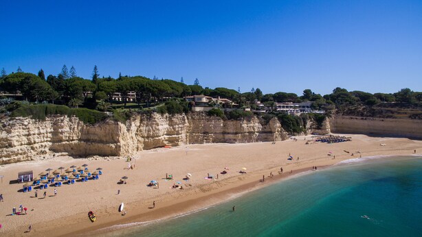 A beach with clear turquoise waters, a sandy shore, and a cliffside with buildings. - Portuguese house with a large private pool and very close to the beach. (Carvoeiro)