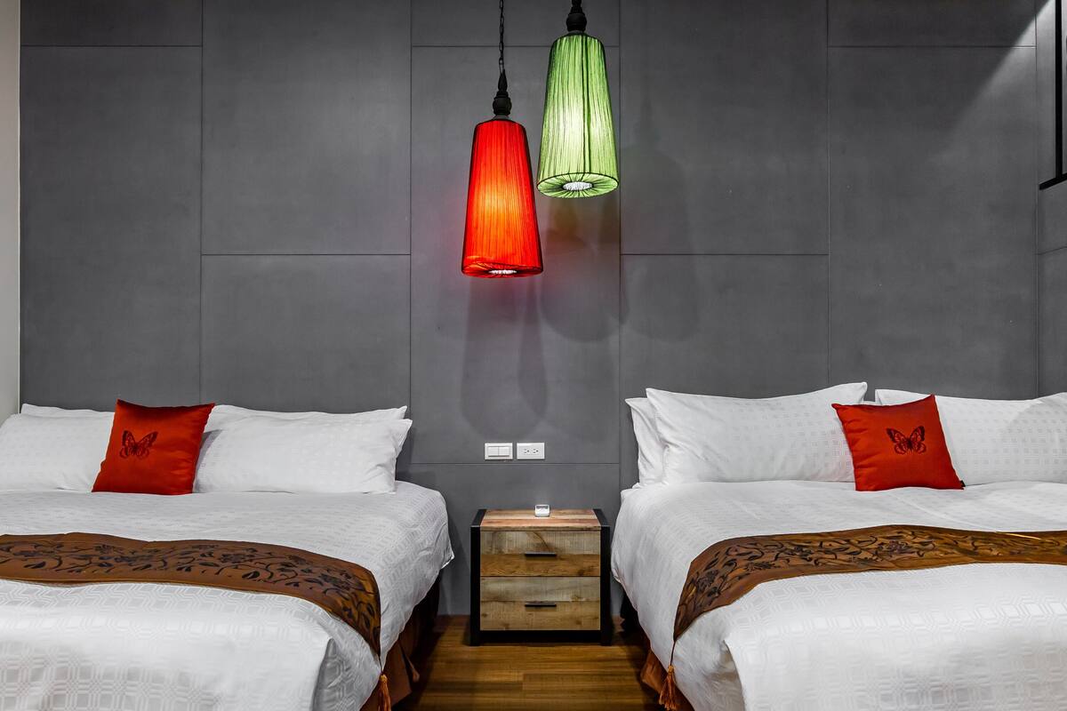 Habitación de hotel con dos camas, una mesita de noche y lámparas colgantes.