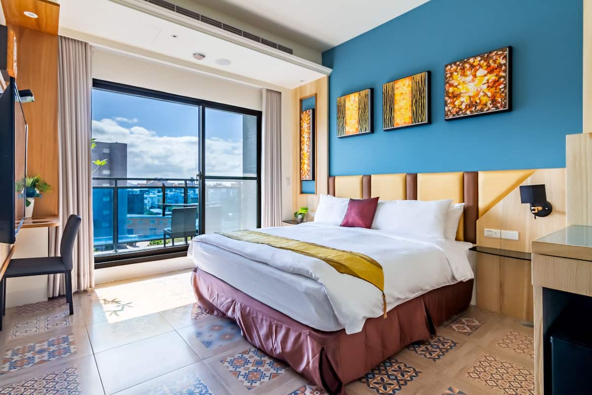 Habitación de hotel moderna con una cama grande, un escritorio y vistas a la ciudad a través de amplios ventanales.