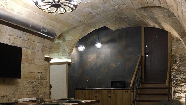 Interior com teto de pedra, mesa de jantar de madeira, sofá de couro e área de cozinha com armários e bancada.