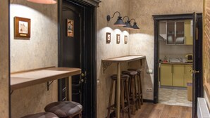 Um corredor estreito com área de bar, incluindo banquetas e balcão, cozinha visível através de uma porta aberta e luminárias fixadas na parede.