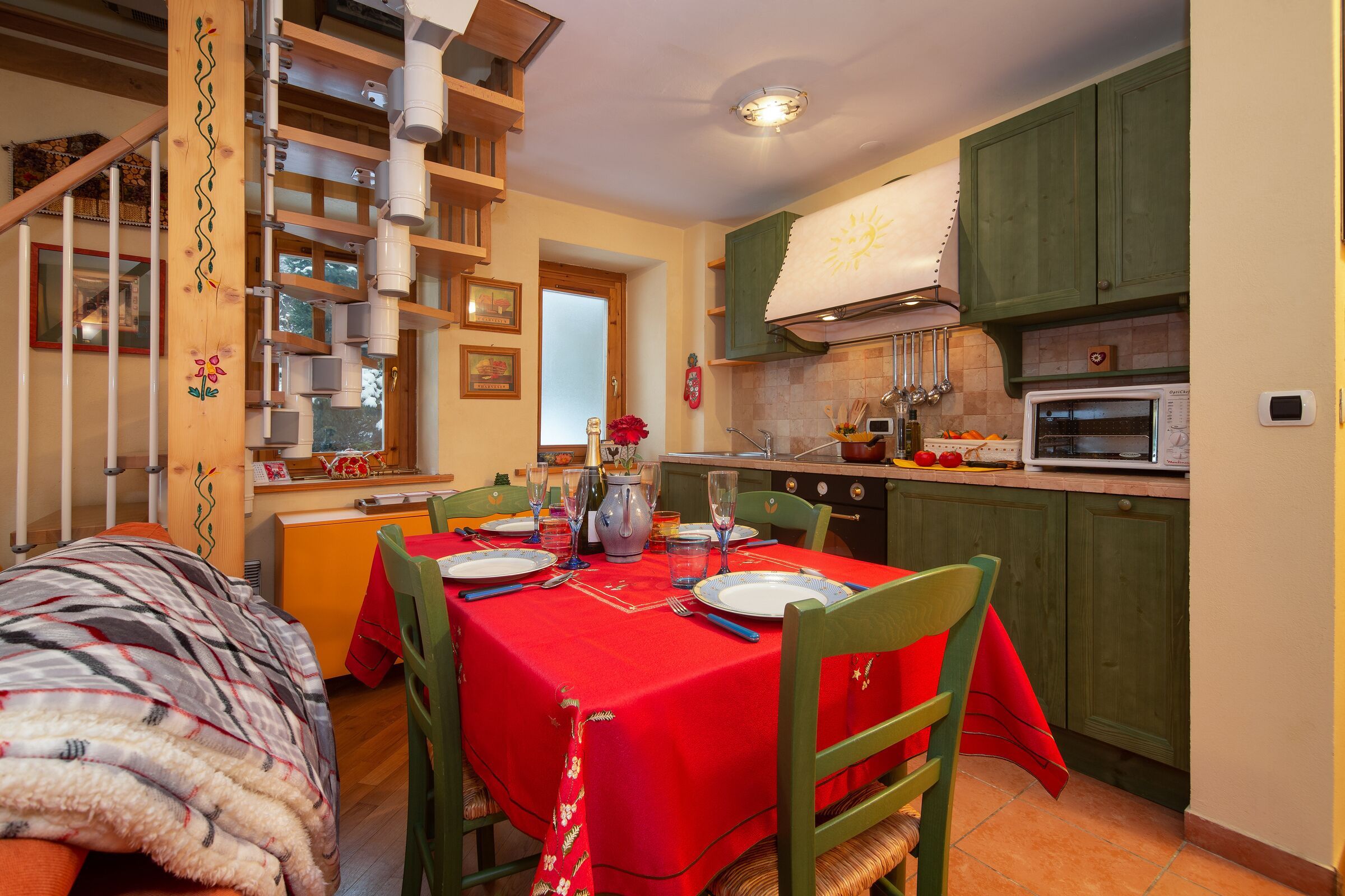 A dining area with a red tablecloth, wooden chairs, and a kitchen in the background.