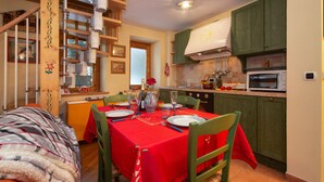 A dining area with a red tablecloth, wooden chairs, and a kitchen in the background. - Apt Beauregard1 Family Duplex Parking & near ski, Les Houches (Chamonix), France (Les Houches (Chamonix))