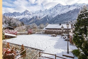 A snow-covered courtyard with a wooden fence, benches, and a building with a snow-covered roof.
