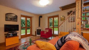 A living room with a television, red armchair, orange sofa, and a staircase. - Apt Beauregard1 Family Duplex Parking & near ski, Les Houches (Chamonix), France (Les Houches (Chamonix))