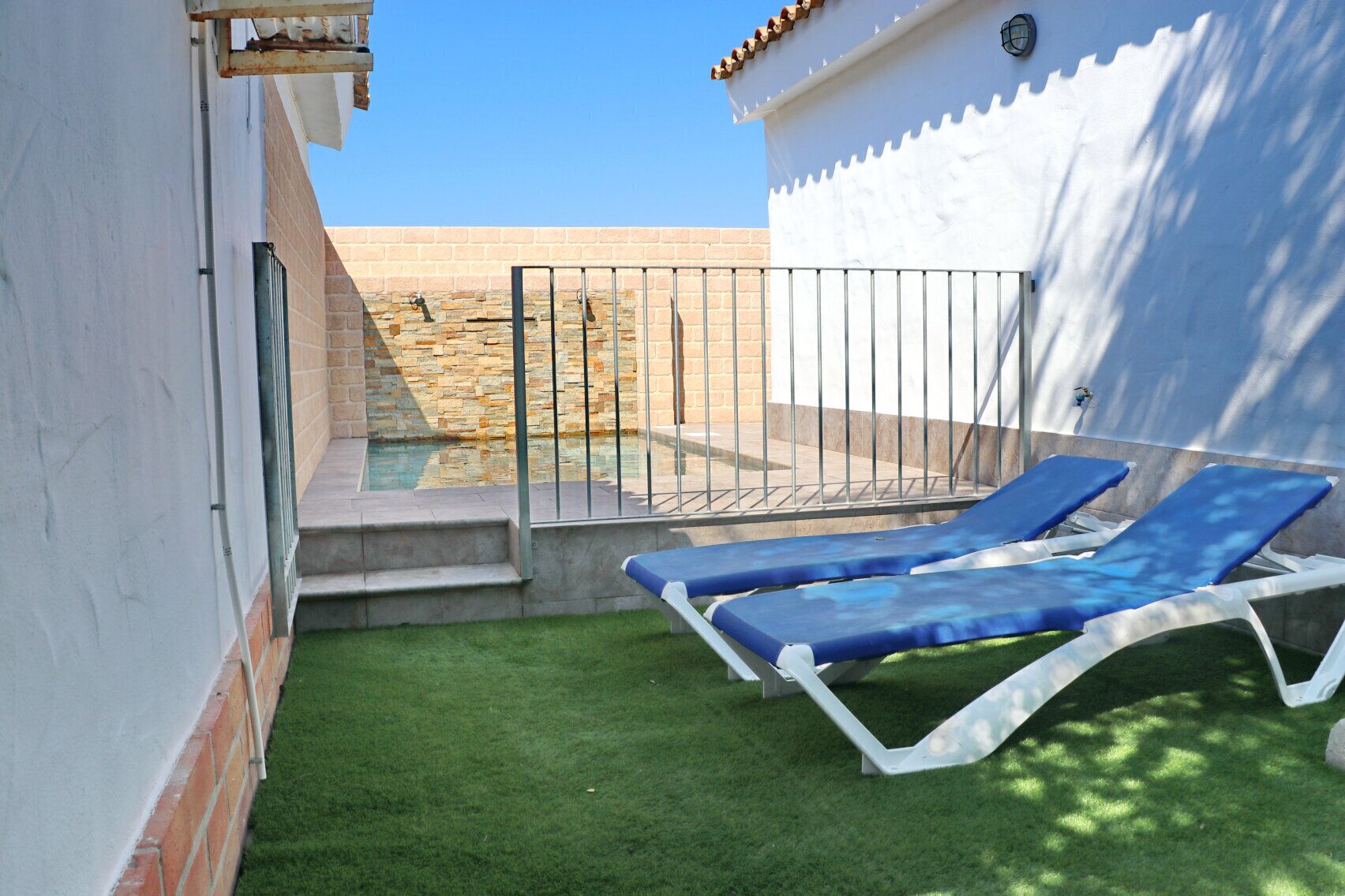 Un pequeño espacio al aire libre con piscina, dos sillones reclinables azules y una pequeña escalera que conduce a un muro de piedra.